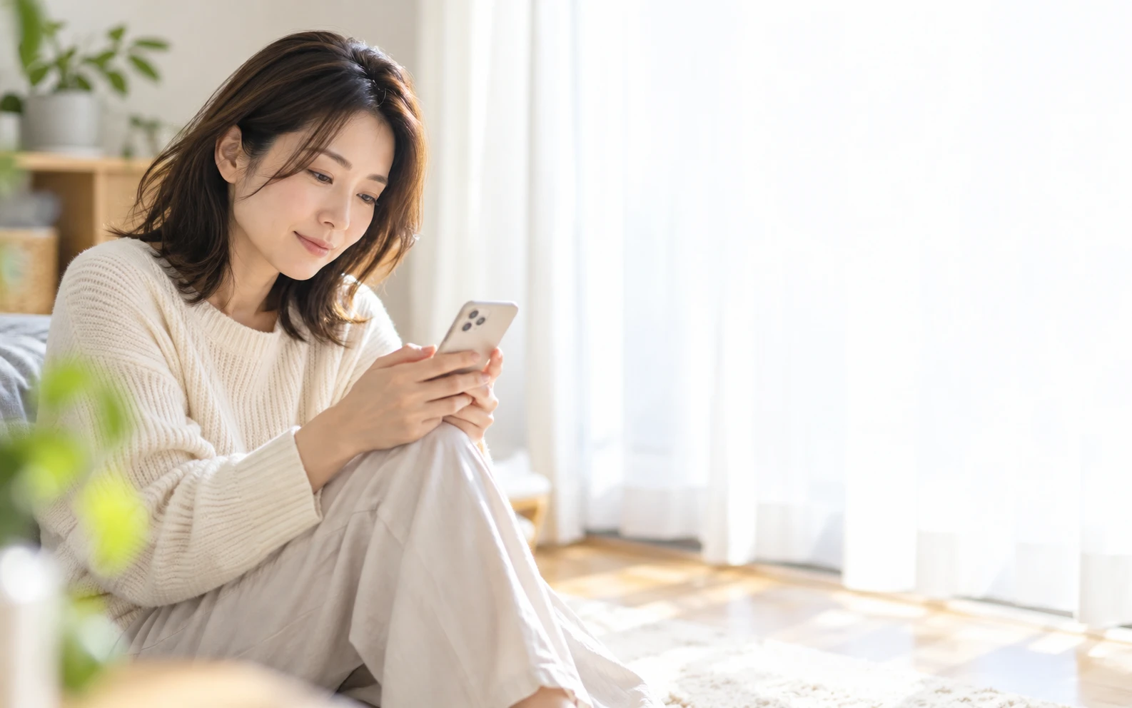 窓辺でスマートフォンを見ながら、考えごとをする女性